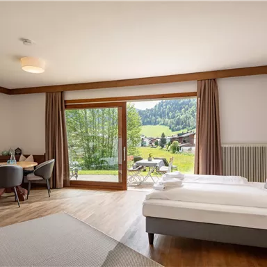 A modern room with two single beds and a view of the green landscape. Large windows let in a lot of light and create an inviting atmosphere.