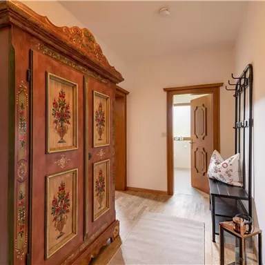 An inviting hallway with a vintage wooden wardrobe and a round mirror. The walls are bright and there is a coat rack for jackets.