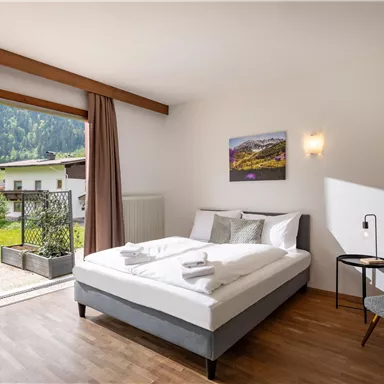A modern bedroom with a double bed and a view of the mountains. There is a balcony with seating and a cozy atmosphere.