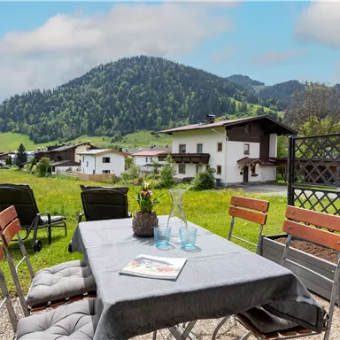 A cozy table outside with chairs and a view of the mountains. The landscape is green and hilly, perfect for relaxing hours.