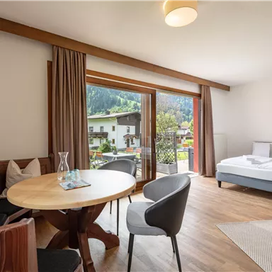 A modern room with a double bed and a dining area. Large windows offer a view of the nature outside.