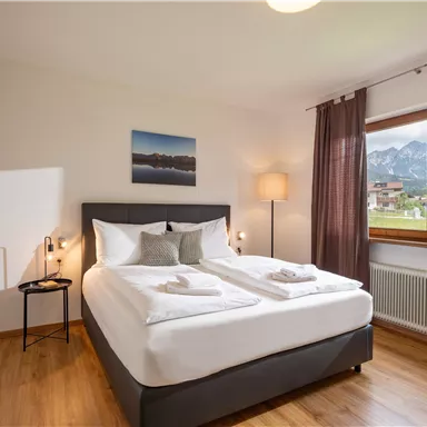 A cozy bedroom with a double bed and a window overlooking the mountains. The warm wood tones and soft lighting create a relaxing atmosphere.