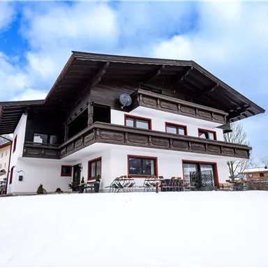 A beautiful chalet in the snow with a large balcony. The sky is clear and the surroundings are picturesque.