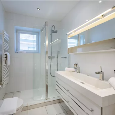 Ein modernes Badezimmer mit einer hellen Dusche und einem eleganten Waschbecken. Die Wände sind in Weiß gehalten, was einen sauberen und zeitlosen Look erzeugt.