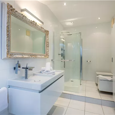 Ein modernes Badezimmer mit eleganten Fliesen und einer Glasdusche. Der große Spiegel verleiht dem Raum zusätzlichen Glanz.