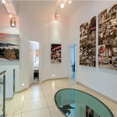 Ein moderner Flur mit hellen Wänden und eleganten Kunstwerken. Der Boden ist aus glänzendem Fliesen und es gibt eine stilvolle Glastischplatte.