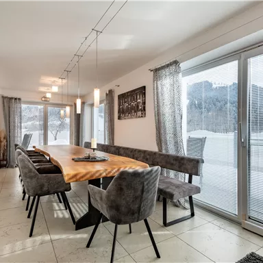 Ein eleganter Essbereich mit einer langen Holztafel und gepolsterten Stühlen. Große Fenster bieten einen Blick auf die winterliche Landschaft.