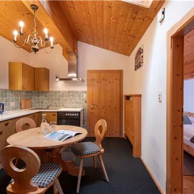 Eine gemütliche Küche mit Holzmöbeln und einem runden Tisch. Der Raum hat eine gemütliche Atmosphäre und Zugang zu einem Schlafzimmer.