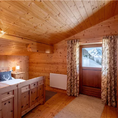 Ein gemütliches Schlafzimmer aus Holz mit einem großen Fenster, das einen Blick auf die Berge bietet. Die Einrichtung ist warm und einladend, ideal für einen entspannten Aufenthalt.