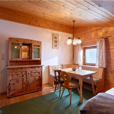 Ein gemütlicher Raum mit Holzverkleidung, einem Esstisch und Stühlen. Im Hintergrund befindet sich eine schöne Anrichte und ein Fenster, das viel Licht hereinlässt.