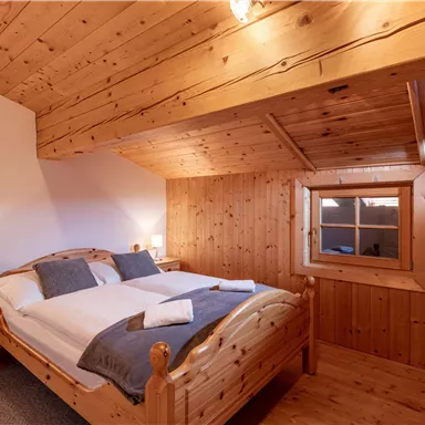Ein gemütliches Schlafzimmer mit einem Holzrahmenbett und zwei Nachttischen. Die Wände und Decke sind ebenfalls aus Holz, mit einem kleinen Fenster, das natürliches Licht hereinlässt.