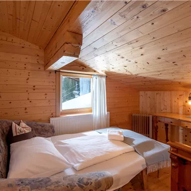 Ein gemütliches Schlafzimmer mit Holzverkleidung und einem Doppelbett. Durch das Fenster fällt Tageslicht und der Raum wirkt warm und einladend.