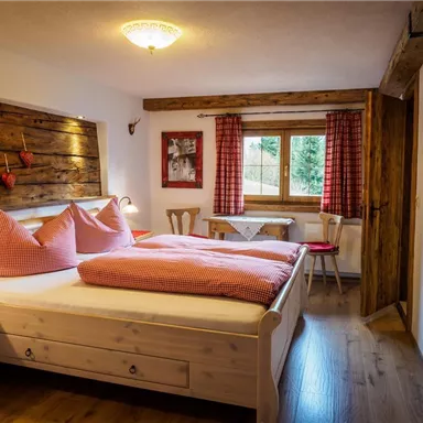 Ein gemütliches Schlafzimmer mit einem Doppelbett, das rot-weiß kariert dekoriert ist. Holzverkleidung und warme Farben schaffen eine einladende Atmosphäre.