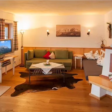 Ein gemütliches Wohnzimmer mit einem grünen Sofa und einem Fernseher. Das Ambiente wird durch warmes Licht und Holzelemente ergänzt.