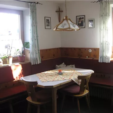 Ein gemütlicher Essbereich mit einer Sitzbank und einem Tisch. Die Wände sind mit Holz verkleidet und es gibt einige Pflanzen und Bilder.