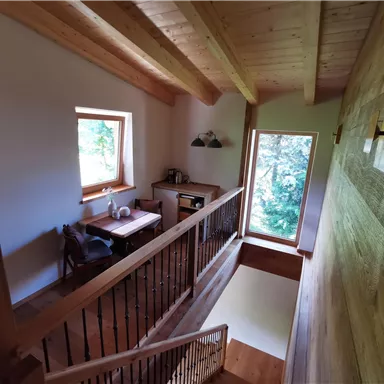 A bright staircase with a wooden railing that leads to a cozy living space. Lots of daylight comes through the windows, and there is a view of the greenery.