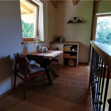 A cozy room with a wooden table and a chair. Natural light comes through the window and offers a view of the greenery.