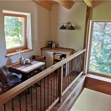 A cozy little kitchen with a table and chairs. Large windows offer a view of the greenery.