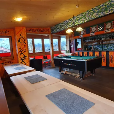 Ein gemütlicher Raum mit bunten Wänden und einem Billardtisch. Tische und Bänke bieten Platz zum Entspannen und Spielen.
