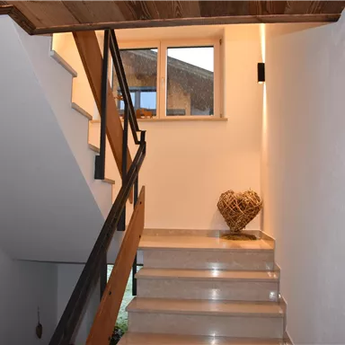 Ein heller Flur mit einer Treppe und Holzdetails. Am Ende der Treppe steht ein dekoratives Herz aus Naturmaterialien.