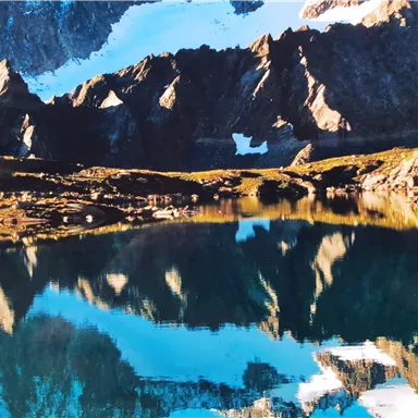 A beautiful mountain landscape with snow-capped peaks and a clear lake. The mountains reflect calmly in the water.