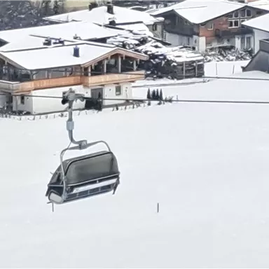 A snow-covered landscape with a cable car gliding over the white snow. In the background, some houses are visible.