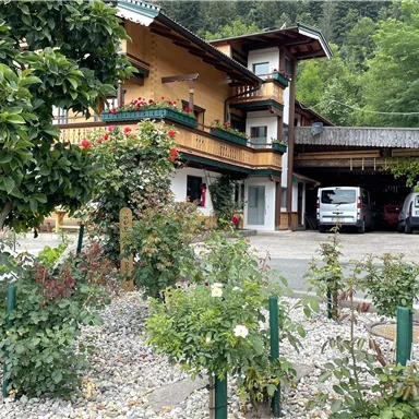 Ein gemütliches Haus mit Balkonen und Blumengärten. Parkplätze sind ebenfalls sichtbar, umgeben von grünen Pflanzen.