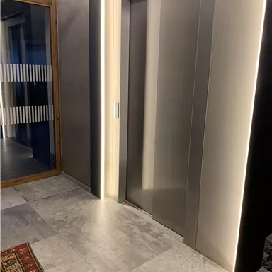 Ein moderner Aufzug in einem eleganten Raum. Der Boden ist mit grauen Fliesen ausgelegt und ein Teppich ergänzt die Einrichtung.