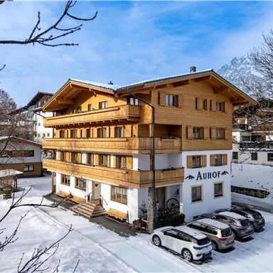 A modern wooden building in a snow-covered landscape. In front of the building are several cars and the sky is clear.