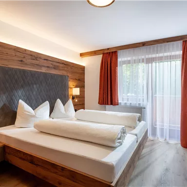 Ein gemütliches Schlafzimmer mit Holzdetails und zwei Einzelbetten. Große Fenster lassen viel Licht herein und die Vorhänge sind in einem warmen Farbton.