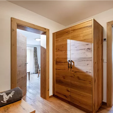 Ein modern gestalteter Flur mit Holzmöbeln und einem offenen Eingang zu einem weiteren Raum. Helle Wände und große Fenster sorgen für viel Licht.