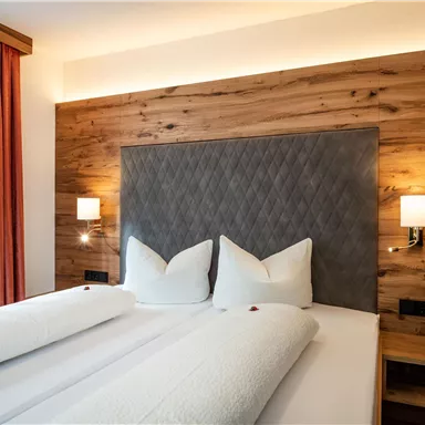 Ein modernes Schlafzimmer mit einem Doppelbett und Holzverkleidung. Die Wände sind hell und mit eleganten Lampen beleuchtet.