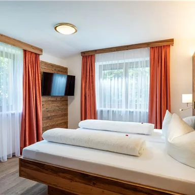 Ein gemütliches Schlafzimmer mit zwei Betten und modernen Holzdetails. Große Fenster lassen viel Licht herein und sorgen für eine freundliche Atmosphäre.