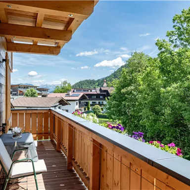 Ein schöner Balkon mit Holzverkleidung und Blick auf die Natur. Bunte Blumen und eine malerische Landschaft sorgen für eine gemütliche Atmosphäre.