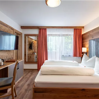 Ein modernes Zimmer mit zwei Betten und Holzdetails. Der Raum ist hell und einladend, mit Fenster und einem Flachbildfernseher.