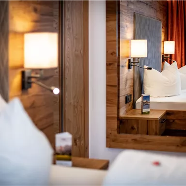 Ein komfortables Hotelzimmer mit Holzdetails und einem großen Spiegel. Im Hintergrund sind ein Bett und gemütliche Kissen sichtbar.