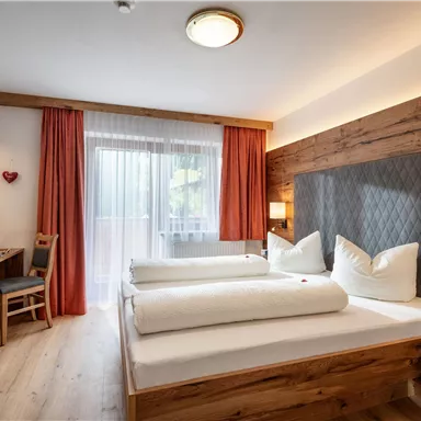 Ein modernes Hotelzimmer mit zwei Betten und warmen Holzelementen. Große Fenster sorgen für viel Licht und einen einladenden Blick nach draußen.