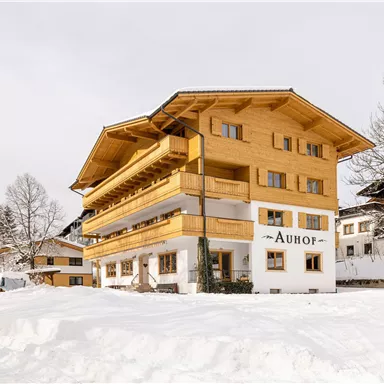 Ein hübsches Holzgebäude im Winter mit schneebedecktem Boden. Der Name "Auhof" ist gut sichtbar.