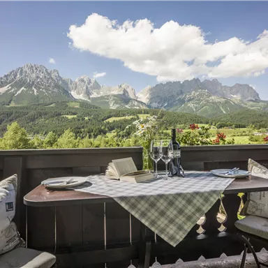 A beautiful table on a terrace overlooking impressive mountains and a green landscape. The sun is shining, and the atmosphere is relaxing.
