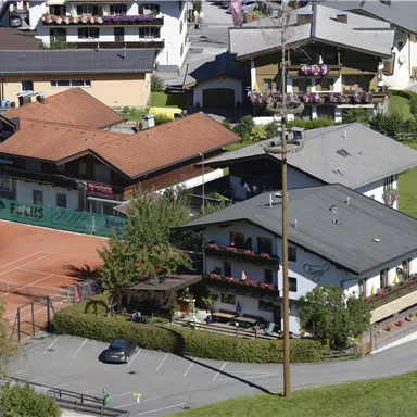 A view of several houses in a quiet environment. In the foreground, there is a tennis court and a parking lot.