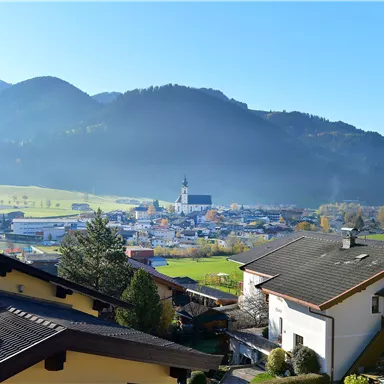 Eine malerische Ansicht eines Dorfes umgeben von Bergen. Der Himmel ist klar und blau, und die Häuser sind in einer friedlichen Landschaft angeordnet.