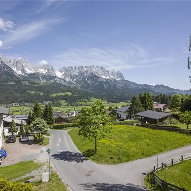 A picturesque landscape with majestic mountains in the background. In the foreground, there is a peaceful village with green meadows and trees.