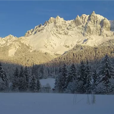 Eine schneebedeckte Berglandschaft mit majestätischen Gipfeln. Der Himmel ist klar und die Sonne beleuchtet die winterliche Szenerie.
