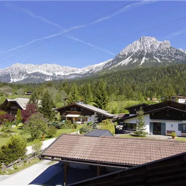 A picturesque landscape with mountain views and traditional houses. Green meadows and a blue sky give the scene a peaceful atmosphere.