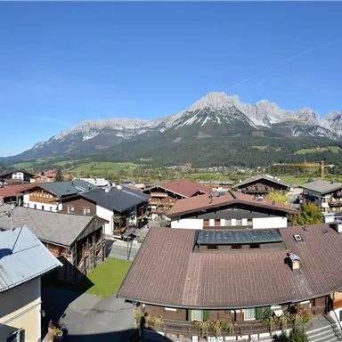Eine malerische Alpenlandschaft mit einem kleinen Dorf und traditionellen Häusern. Im Hintergrund erheben sich majestätische Berge unter einem klaren blauen Himmel.
