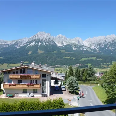 A picturesque landscape with majestic mountains in the background. In the foreground stands a cozy house surrounded by trees and meadows.