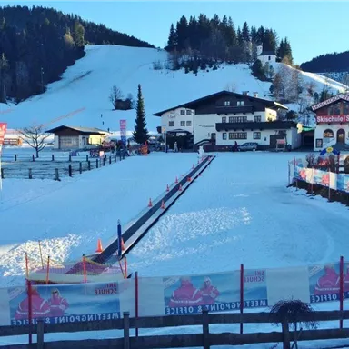 A snowy landscape with a prepared ski course. In the background, traditional alpine buildings and trees can be seen.