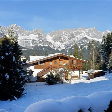 An idyllic chalet in a snow-covered landscape. In the background, impressive mountain peaks can be seen.