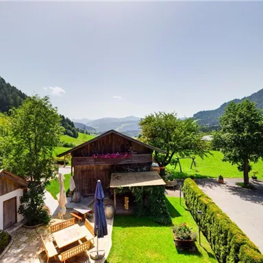 A picturesque landscape with a traditional wooden house and green meadows. In the background, gentle mountains and a clear sky can be seen.