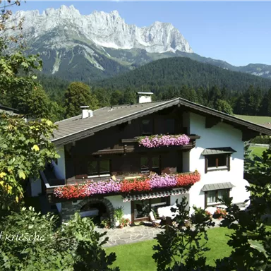 A beautiful house with colorful flower balconies in the midst of a picturesque mountain landscape. The surroundings are green and surrounded by mountains.